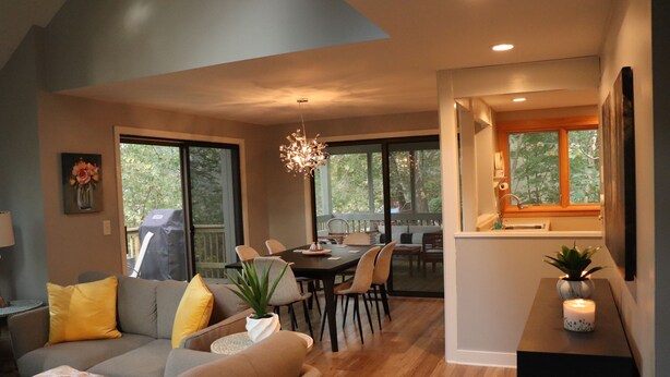 A modern living room with a gray sofa, yellow cushions, a dining area with a wooden table and chairs, and a kitchen with a window. - Quiet & Peaceful (Galena)