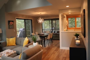 A modern living room with a gray sofa, yellow cushions, a dining area with a wooden table and chairs, and a kitchen with a window. - Quiet & Peaceful (Galena)
