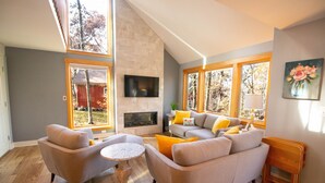 A modern living room with a fireplace, large windows, and a flat-screen TV mounted on the wall. - Quiet & Peaceful (Galena)