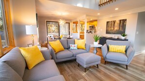 A modern living room with a grey sectional sofa, two armchairs, and a small side table. A dining area is visible in the background with a chandelier. - Quiet & Peaceful (Galena)