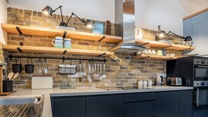 A modern kitchen with a brick wall, wooden shelves, and various kitchen appliances. - 3 bedroom accommodation in Llanboidy (Llanboidy)
