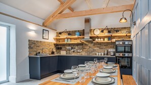 A modern kitchen with a wooden table set for dining, a brick backsplash, and built-in appliances. - 3 bedroom accommodation in Llanboidy (Llanboidy)