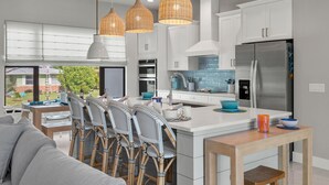 Una cocina moderna con armarios blancos, un refrigerador de acero inoxidable y una zona de comedor con sillas de mimbre y una mesa de madera.