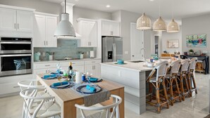 Una cocina moderna con armarios blancos, electrodomésticos de acero inoxidable y una isla central con taburetes para bar.