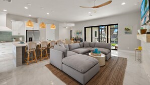 Una cocina moderna con armarios blancos, una isla grande y un comedor con sillas de mimbre.