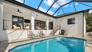 Una casa moderna con piscina, mobiliario exterior y un porche cubierto.