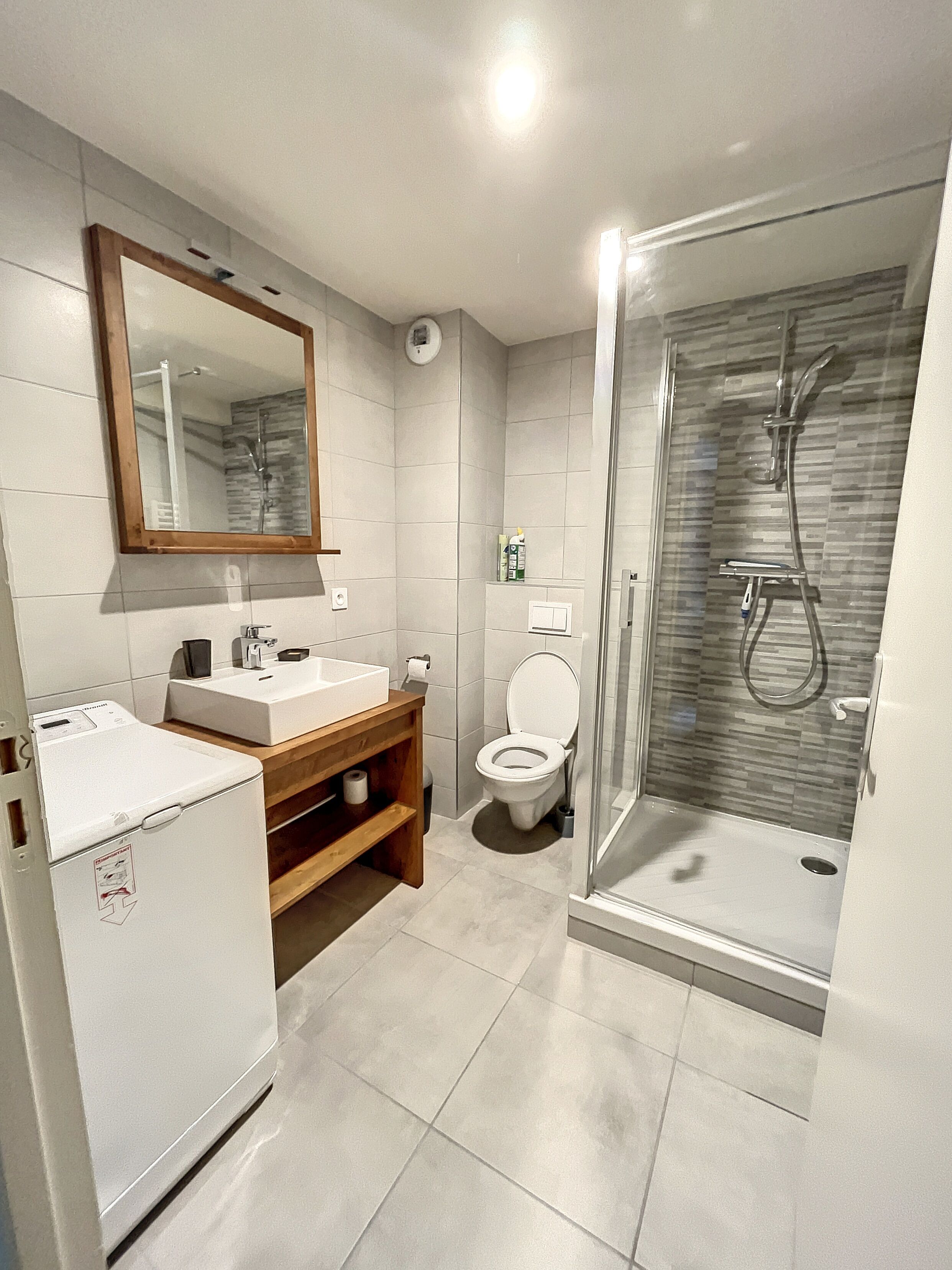 Une salle de bain moderne avec une douche à parois de verre, des toilettes et un lavabo avec un meuble-vasque en bois.