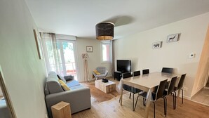 Uma sala de estar moderna com sofá, uma mesa de jantar com cadeiras, televisão e uma luminária.
