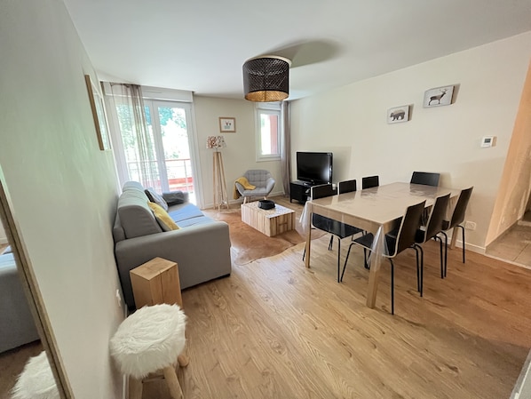A modern living room with a sofa, a dining table with chairs, a TV, and a lamp.