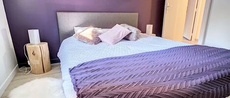A bedroom with a bed, a nightstand, a wall clock, and a door.