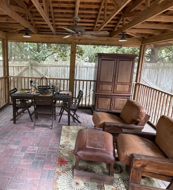 Une terrasse extérieure avec une table en bois, des chaises, un meuble et un ventilateur de plafond.