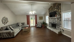 A living room with a stone fireplace, a sofa, a coffee table, and a television. - Preakness Corner, Cheerful, cozy 4 bedroom home (Marietta)