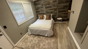 A bedroom with a bed, a window with blinds, a wooden accent wall, a small round table, and a ceiling fan. - Preakness Corner, Cheerful, cozy 4 bedroom home (Marietta)