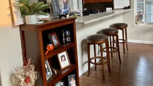 A spacious kitchen with wooden cabinets, a marble countertop, and a large mirror. There are wooden stools and a potted plant on the counter. - Spacious Custom Retreat with a Pool! (Central Point)