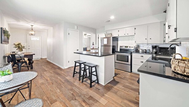 Une cuisine moderne avec des meubles blancs, un îlot central doté de tabourets et un coin repas avec une table et des chaises.
