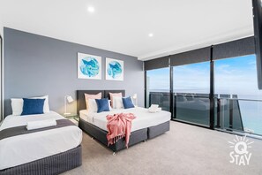 Enjoy ocean views from the large window and balcony, featuring two beds with comfortable bedding and artwork on the walls.