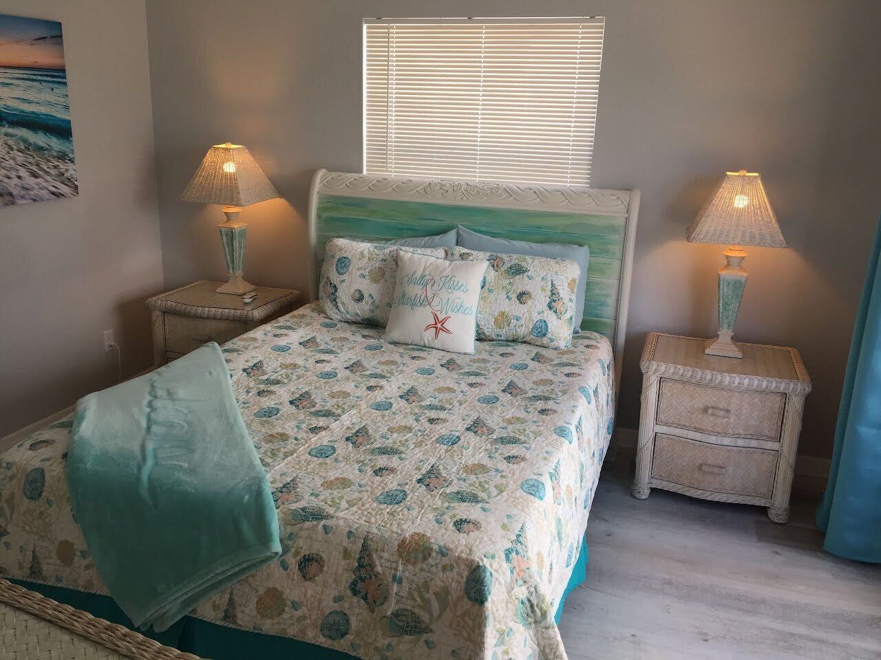 A bedroom with a bed, two bedside tables, a nightstand, a window with blinds, and a wall-mounted picture.