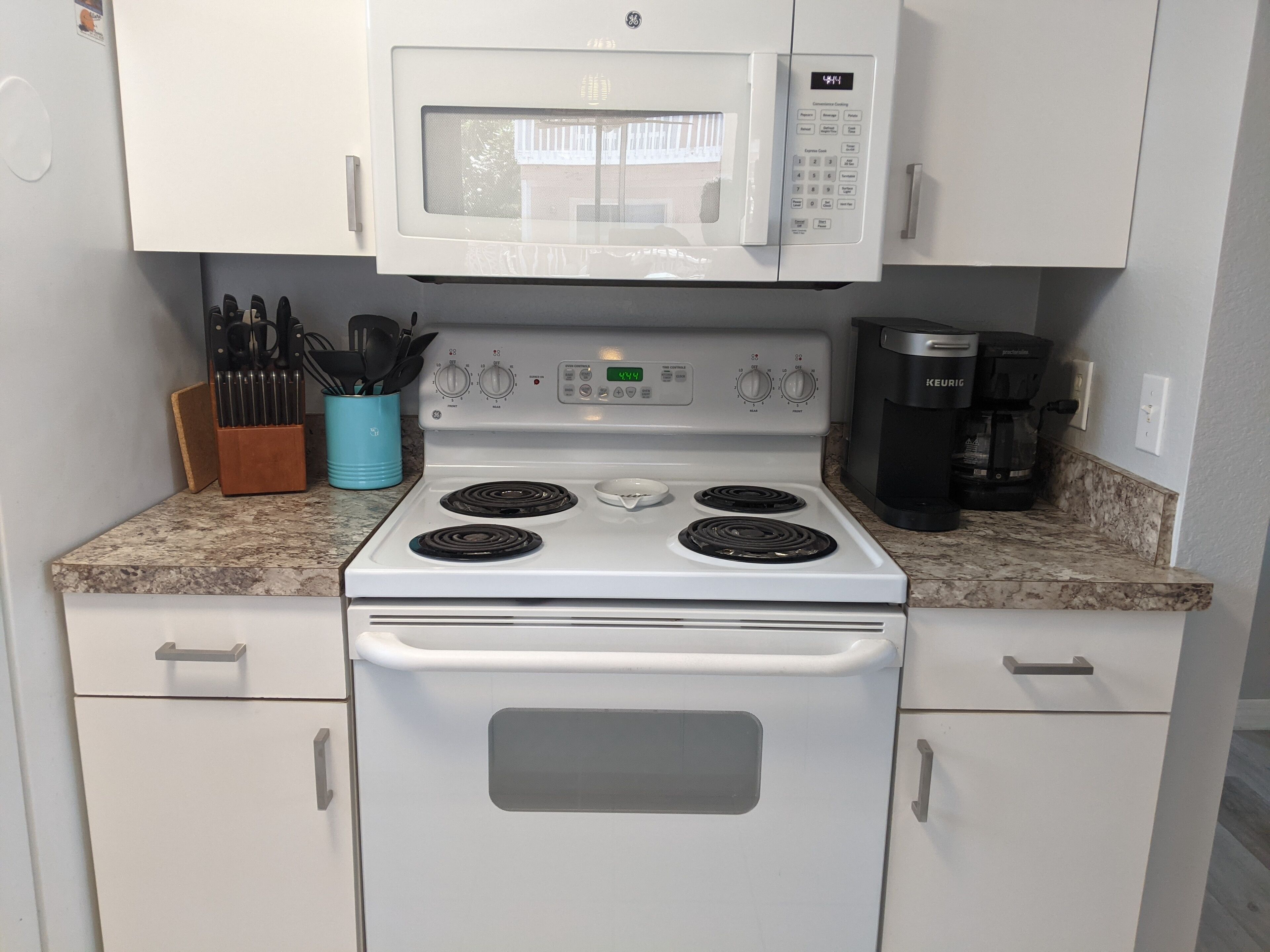 A compact kitchen with a white stove, microwave, and coffee maker.