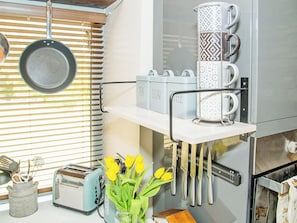 A kitchen with a hanging pot rack, a coffee machine, a toaster, and a vase with flowers.