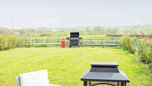 Un espacio al aire libre con césped, una parrilla, una mesa y un banco.