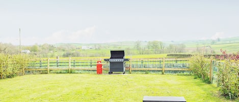 A grassy outdoor area with a barbecue grill, a table, and a bench.