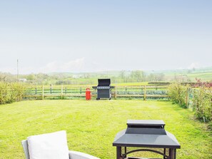 A grassy outdoor area with a barbecue grill, a table, and a bench.