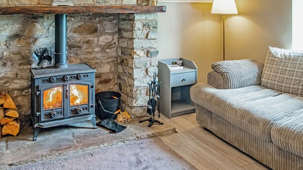 Una habitación acogedora con chimenea de piedra, un sofá, una lámpara y un reloj en la pared.