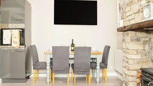Un comedor con una mesa, sillas, un televisor de pantalla plana, un refrigerador y una chimenea de piedra.