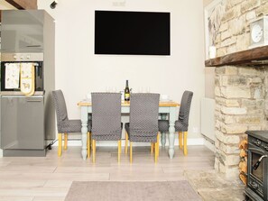 A dining area with a table, chairs, a flat-screen TV, a refrigerator, and a stone fireplace.