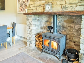 A stone fireplace with a wood-burning stove, a clock, and a rustic wooden shelf above it.