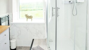 Un baño con cabina de ducha de vidrio, una ventana que da a un área cercada y una pequeña figura decorativa de animal en el alféizar.
