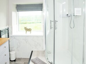 A bathroom with a glass shower enclosure, a window with a view of a fenced area, and a small decorative animal figure on the windowsill.
