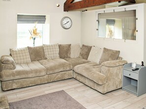 A sectional sofa with a plaid pattern, a wooden floor, a clock on the wall, and a window with blinds.