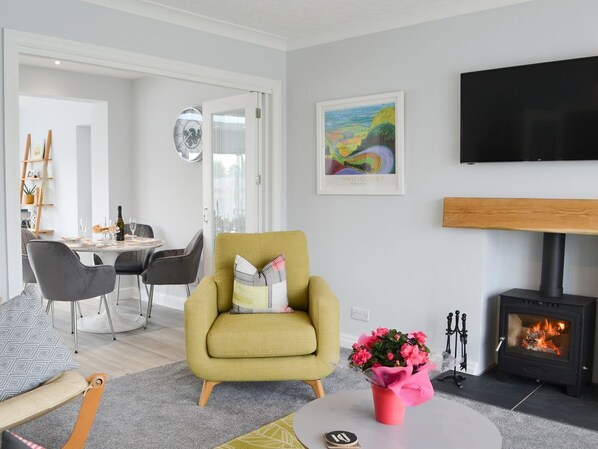 Ein modernes Wohnzimmer mit einem gelben Sessel, einem Kamin, einem Essbereich und einem Flachbildfernseher.