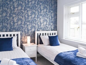 Ein Schlafzimmer mit zwei Betten, weißen Kopfteilen und einer blauen Wand mit Struktur.