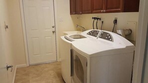 Compact laundry room with a front-loading washing machine and sink, complete with a door and storage above.