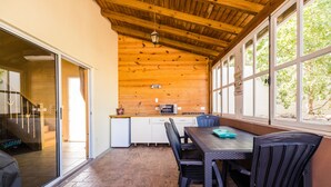 A wooden-paneled room with a dining table and chairs, a kitchen area with appliances, and large windows.