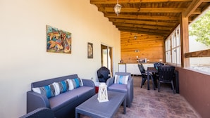 An outdoor patio with wicker furniture, a wooden ceiling, and a view of the kitchen through large windows.