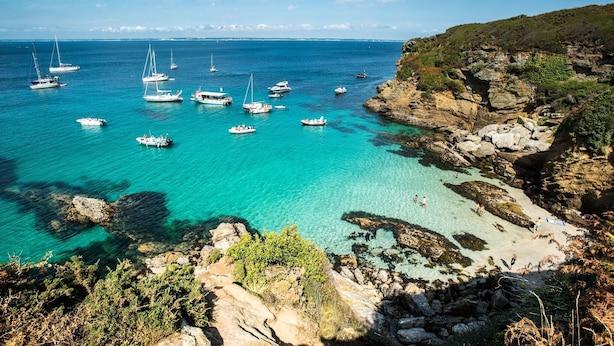 Una zona costera con aguas turquesas cristalinas, acantilados rocosos y barcos anclados cerca de la orilla.