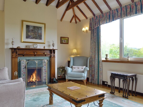 A cozy living room with a fireplace, a comfortable armchair, a wooden coffee table, and a view through a window. - 3 bedroom accommodation in Stonehaven (Stonehaven)