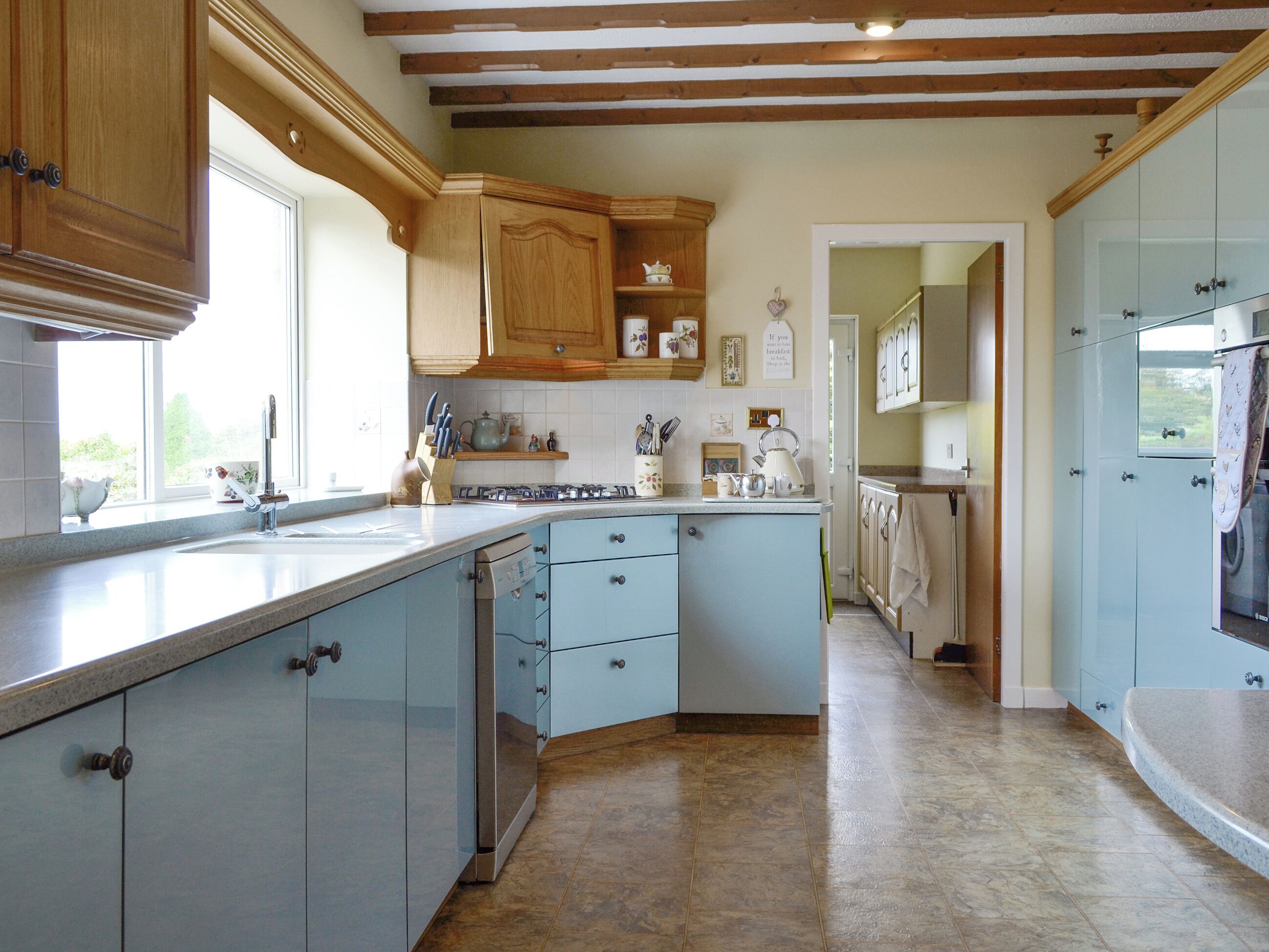 A kitchen with light blue cabinets, a wooden ceiling, and a window providing natural light.