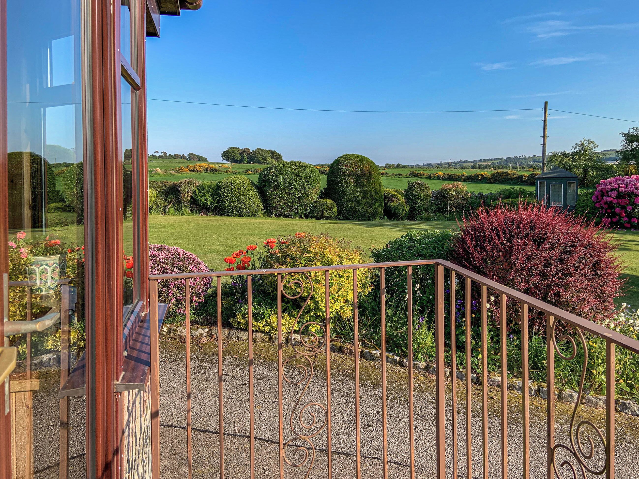 A garden view with a gravel pathway, manicured hedges, and a gazebo.