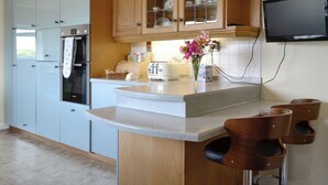 A modern kitchen with wooden cabinets, a built-in oven, a toaster, and a flat-screen TV mounted on the wall. - 3 bedroom accommodation in Stonehaven (Stonehaven)