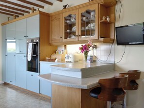 A modern kitchen with wooden cabinets, a built-in oven, a toaster, and a flat-screen TV mounted on the wall. - 3 bedroom accommodation in Stonehaven (Stonehaven)