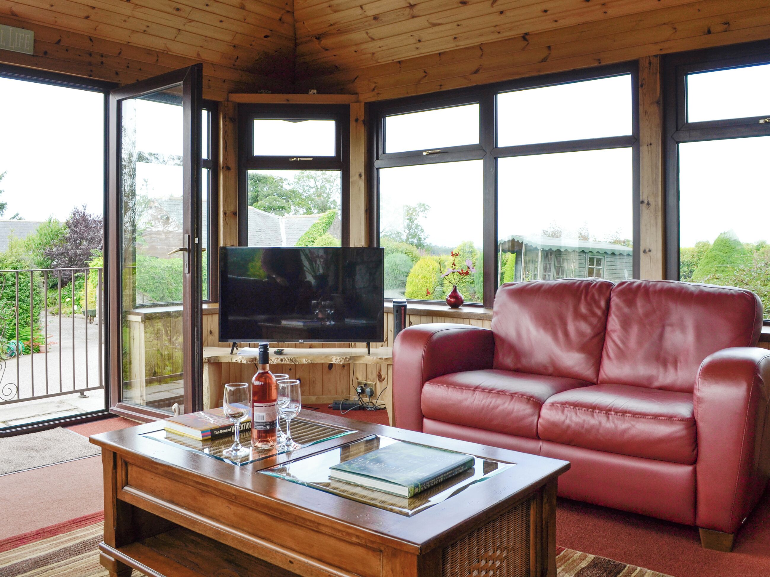 A cozy living room with a leather sofa, a flat-screen TV, and a coffee table with books and glasses.