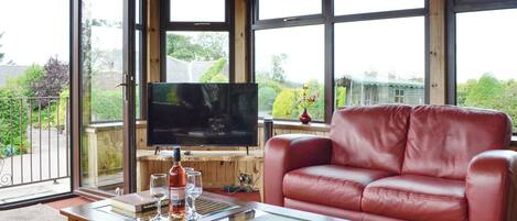 A cozy living room with a leather sofa, a flat-screen TV, and a coffee table with books and glasses.