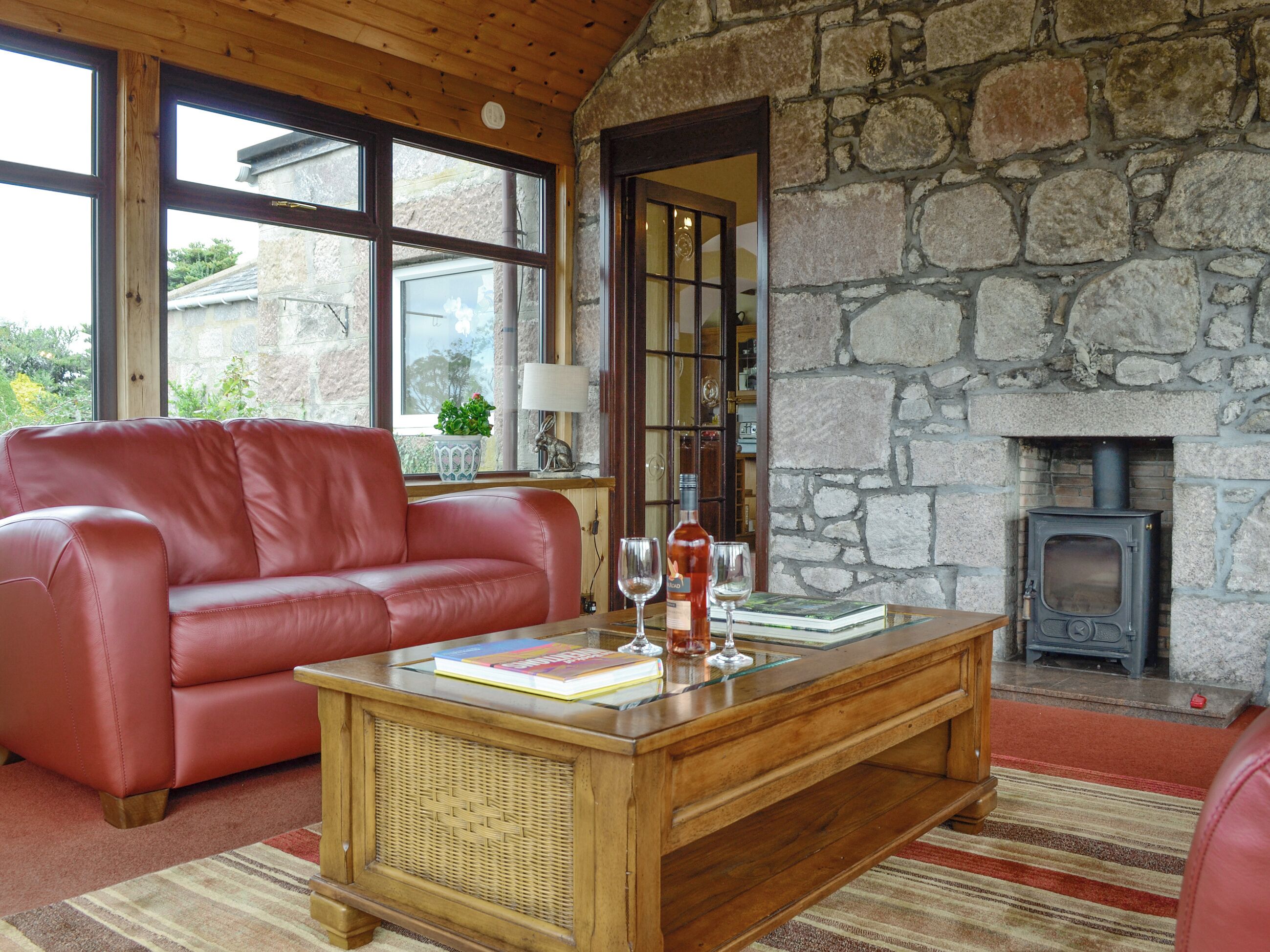 A cozy living room with a stone wall, a red leather sofa, a wooden coffee table, and a fireplace.