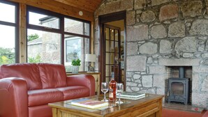 A cozy living room with a stone wall, a red leather sofa, a wooden coffee table, and a fireplace. - 3 bedroom accommodation in Stonehaven (Stonehaven)