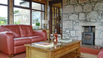 A cozy living room with a stone wall, a red leather sofa, a wooden coffee table, and a fireplace.