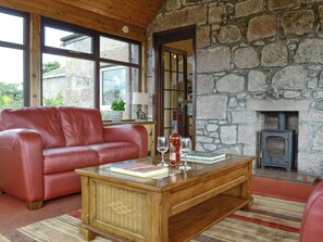 A cozy living room with a stone wall, a red leather sofa, a wooden coffee table, and a fireplace. - 3 bedroom accommodation in Stonehaven (Stonehaven)